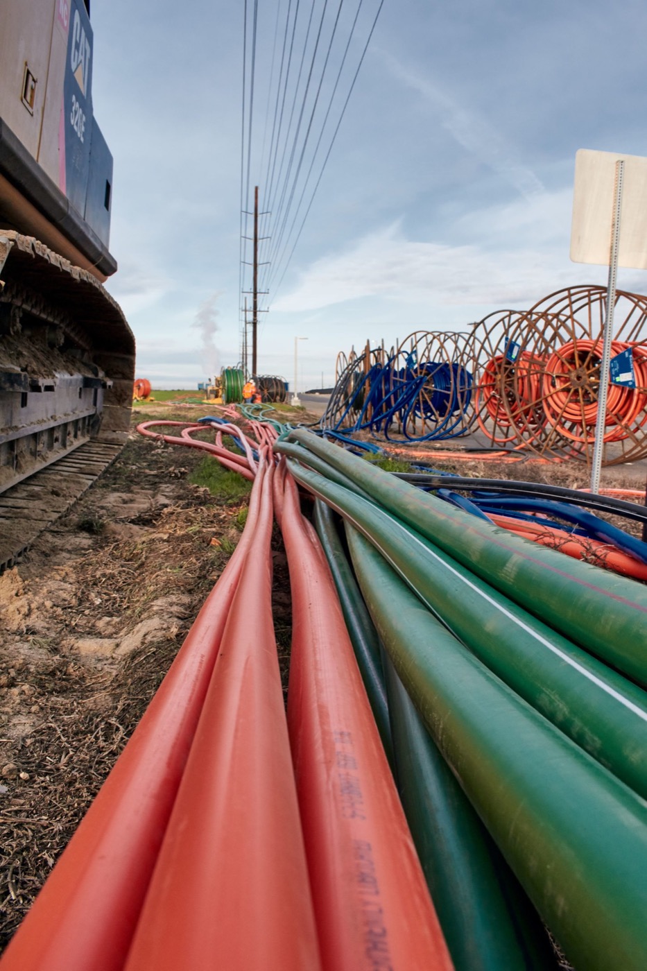 Bundled conduit runs beside a row of cable reels at a staging yard